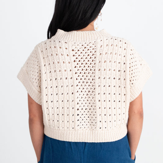 Woman wearing a beige crochet top and blue pants on a white background