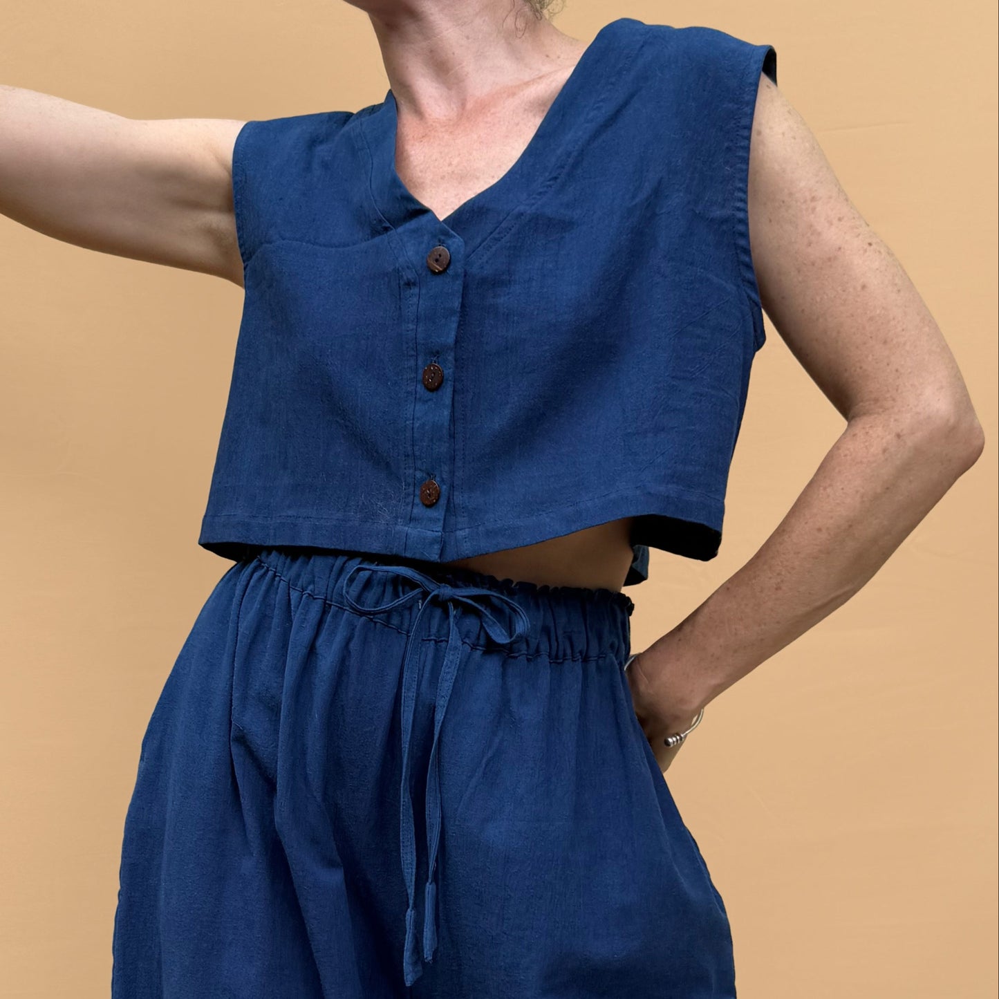 Woman wearing a blue sleeveless top and wide-leg pants against a beige background