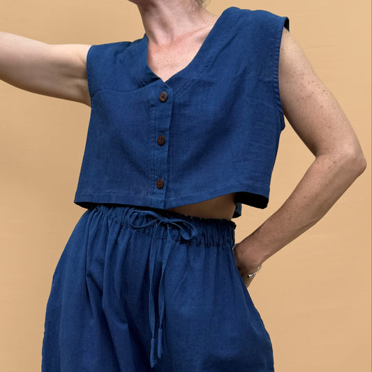 Woman wearing a blue sleeveless top and wide-leg pants against a beige background