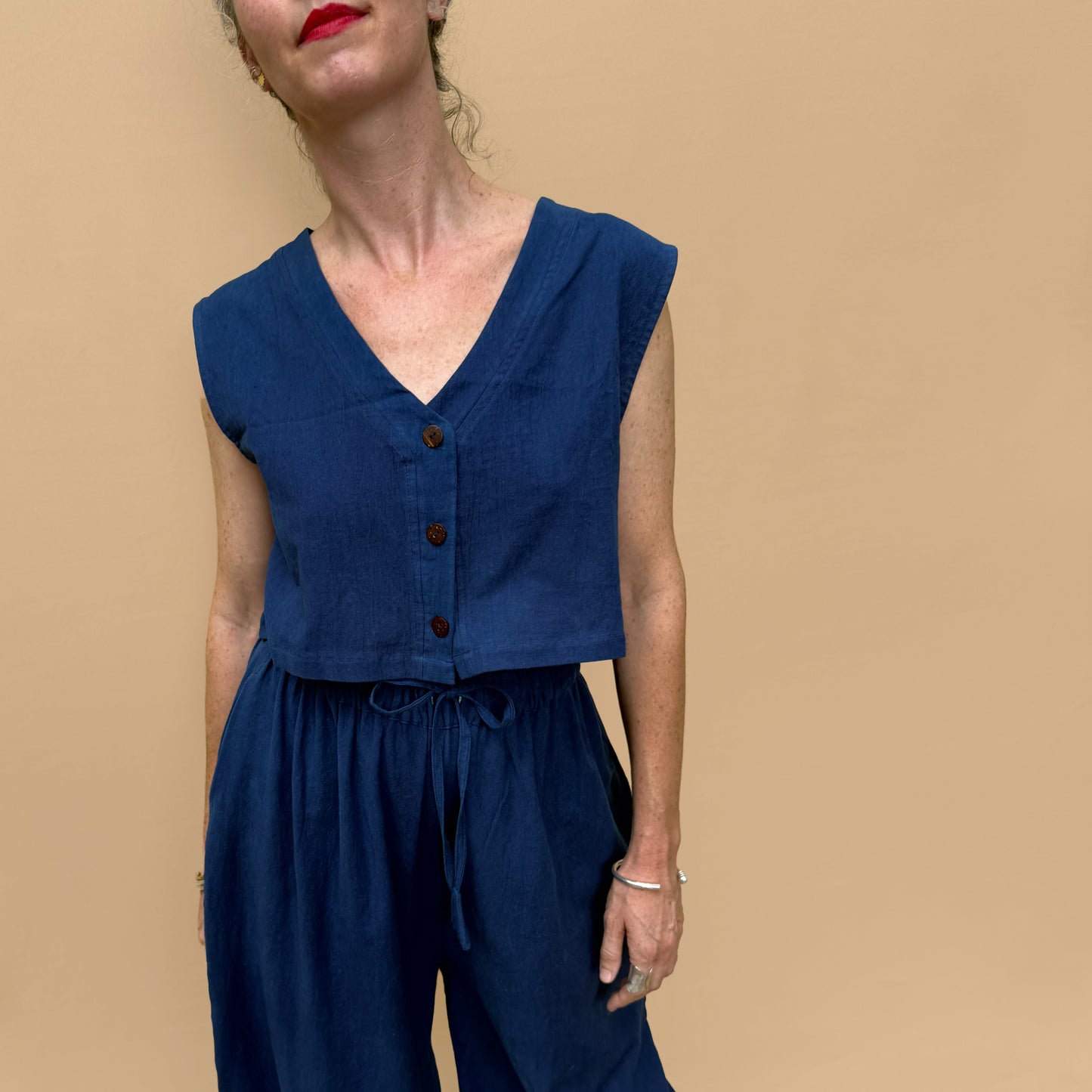 Woman wearing a blue sleeveless top and wide-leg pants against a beige background