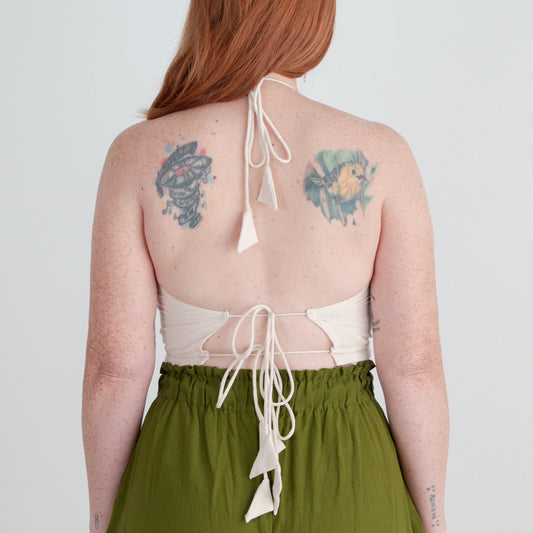 Person wearing a white top with open back and green pants on a plain background