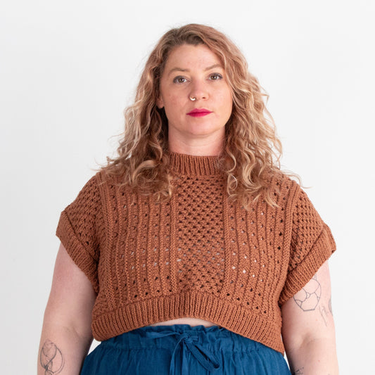 Woman wearing a brown knitted top and blue pants on a white background