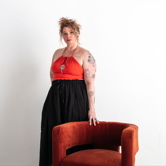 Person wearing a red top and black skirt standing next to an orange chair against a white background
