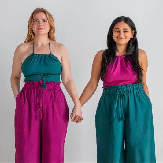 Two women holding hands wearing matching outfits with teal and pink tops and purple pants.