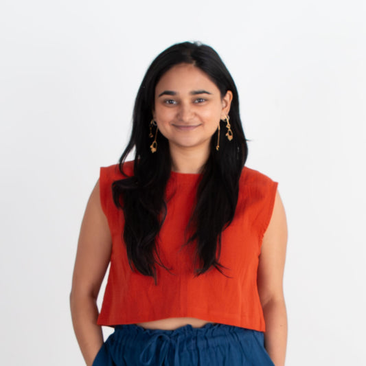 Woman wearing an orange top and blue pants standing against a white background