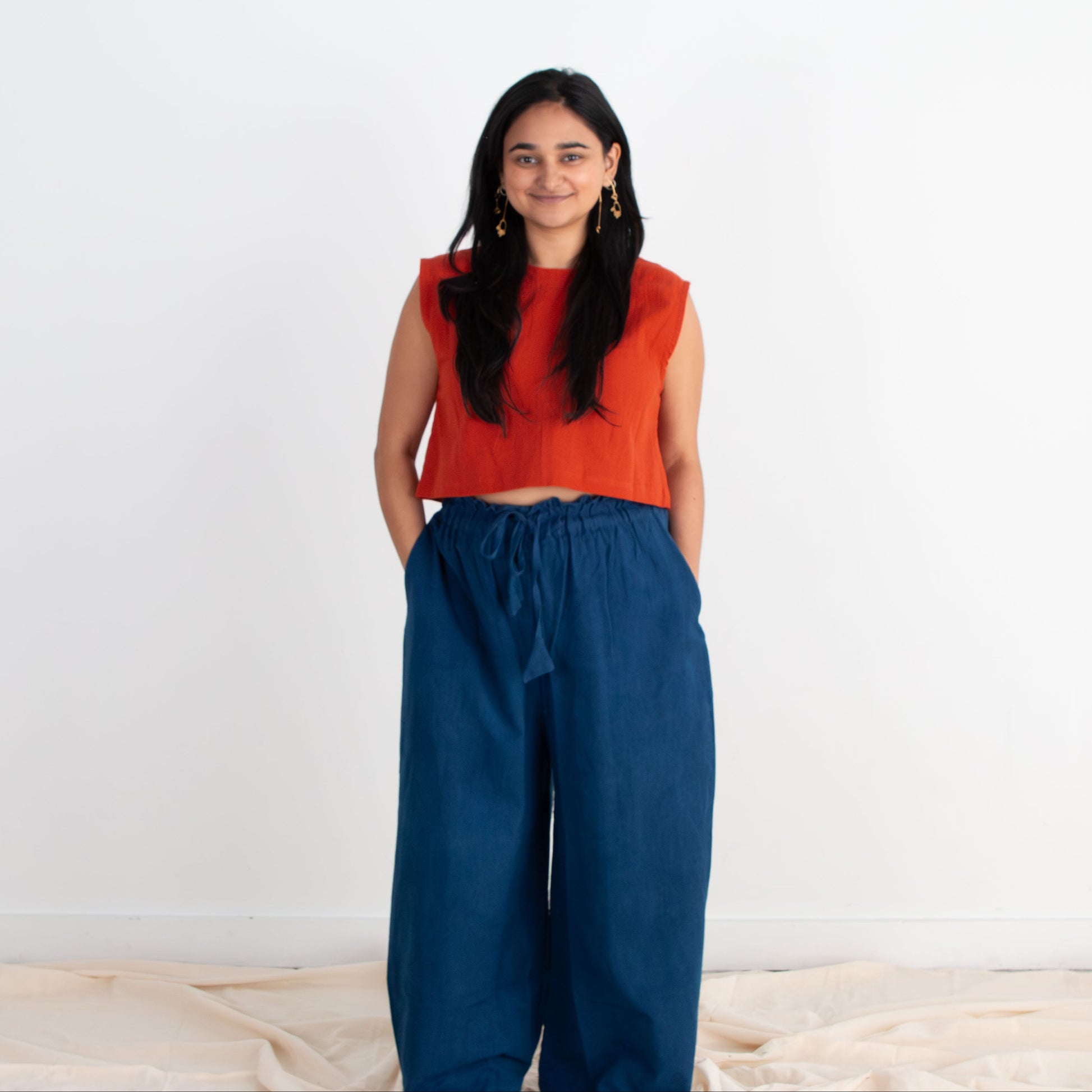 Woman wearing an orange top and blue pants standing against a white background