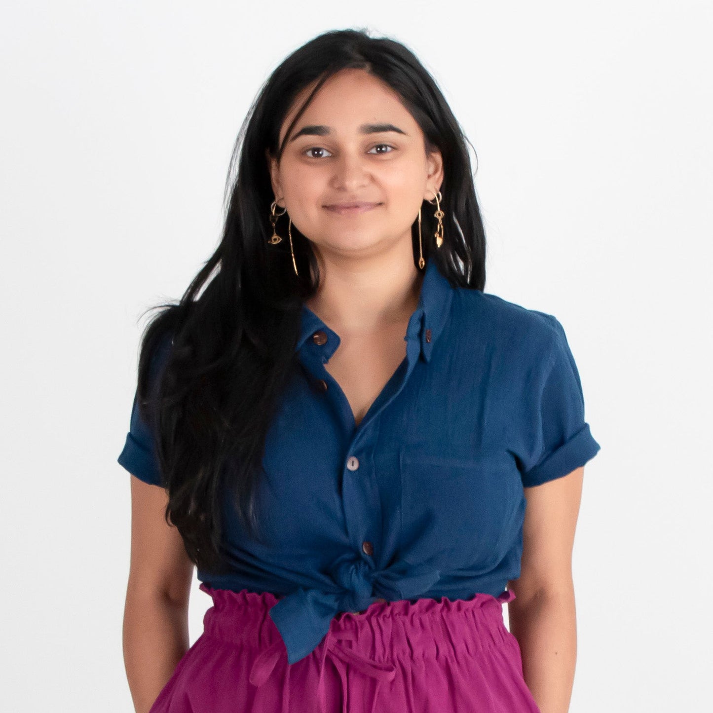 Woman wearing a blue shirt and purple pants standing against a white background