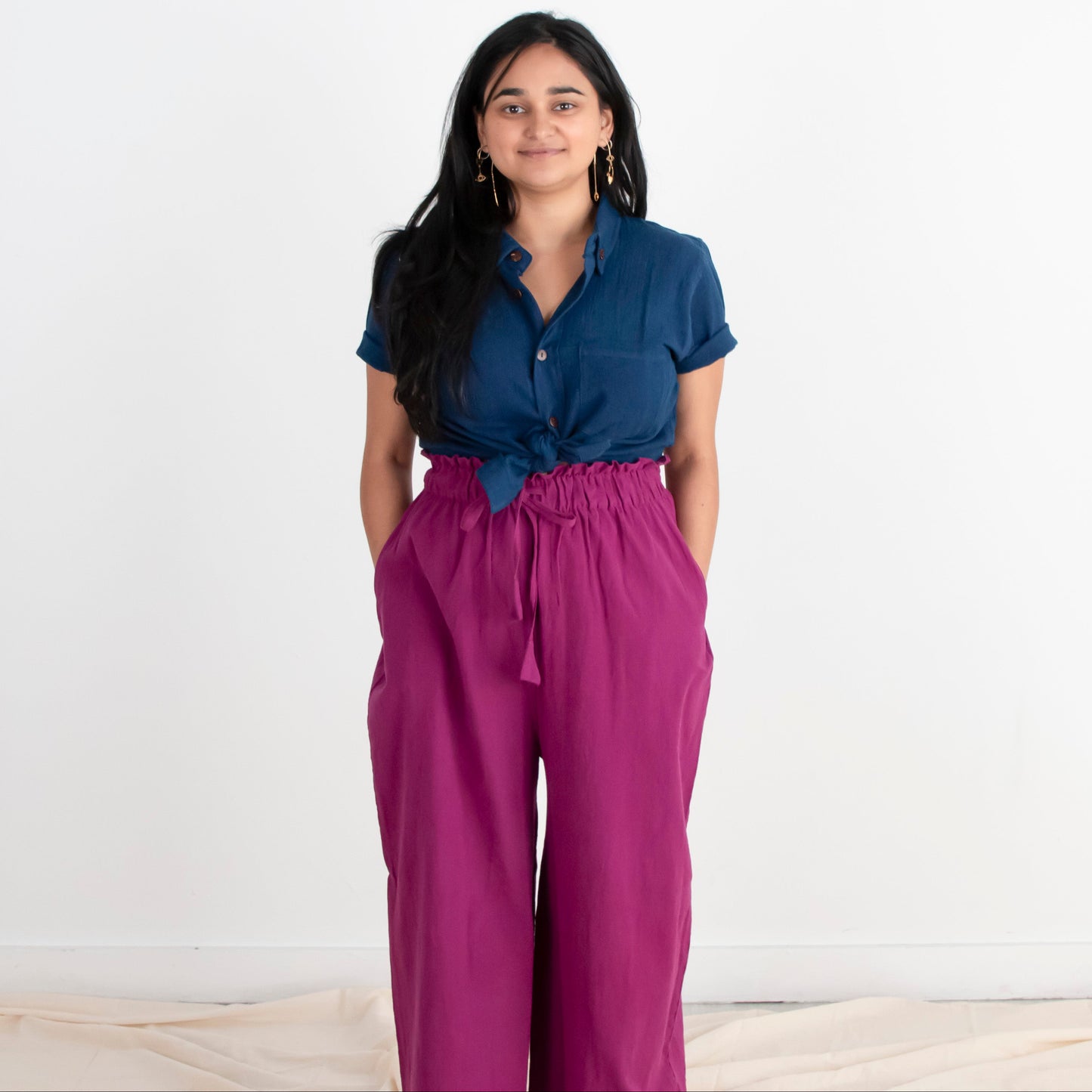 Woman wearing a blue shirt and purple pants standing against a white background