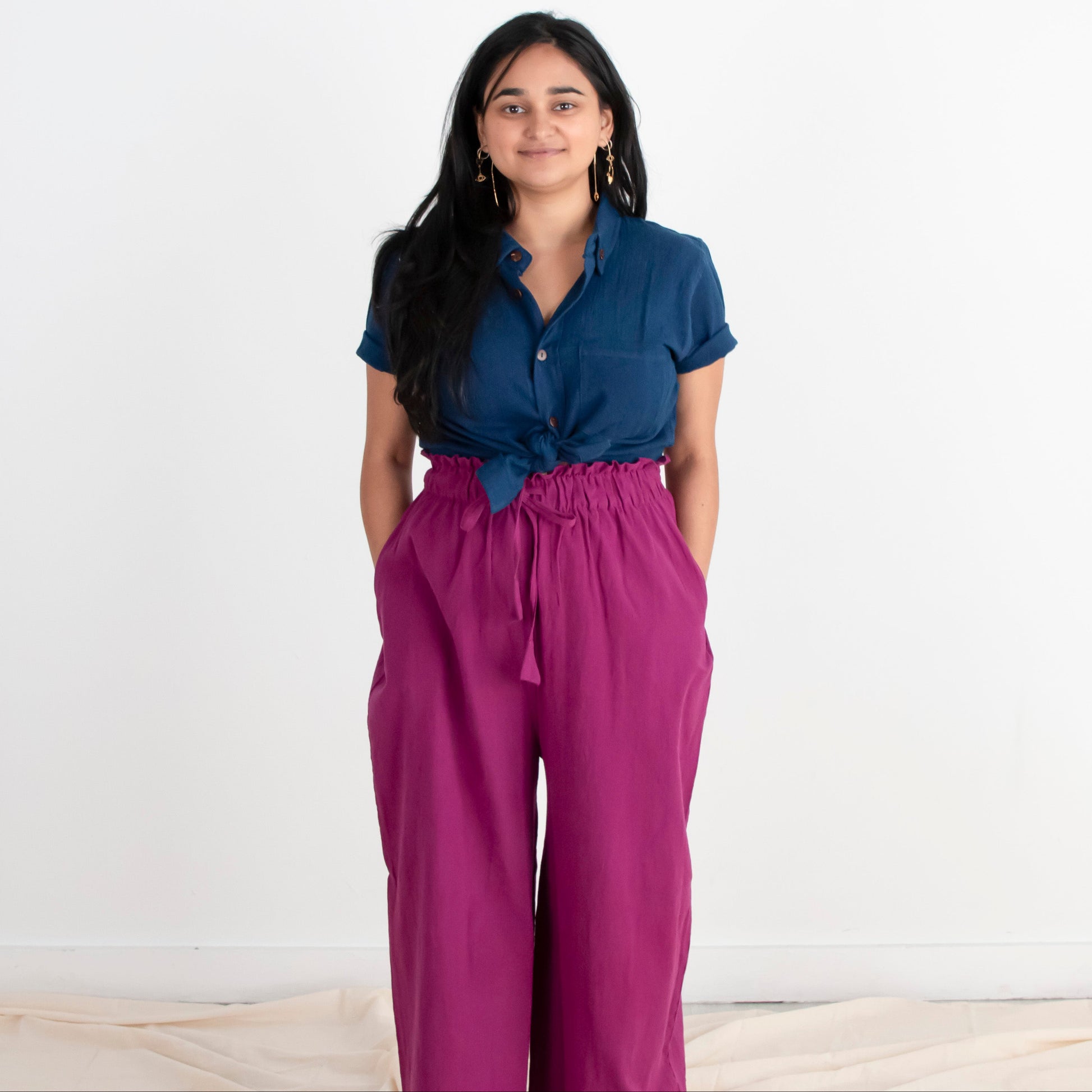 Woman wearing a blue shirt and purple pants standing against a white background