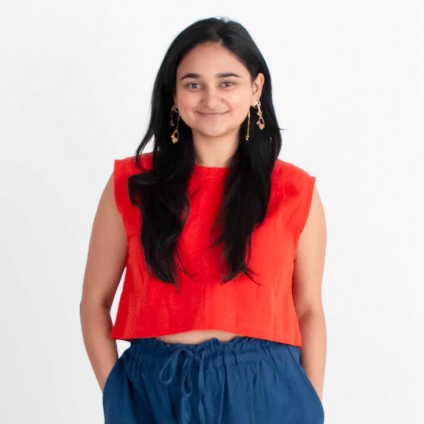 Woman wearing a red top and blue pants standing against a white background