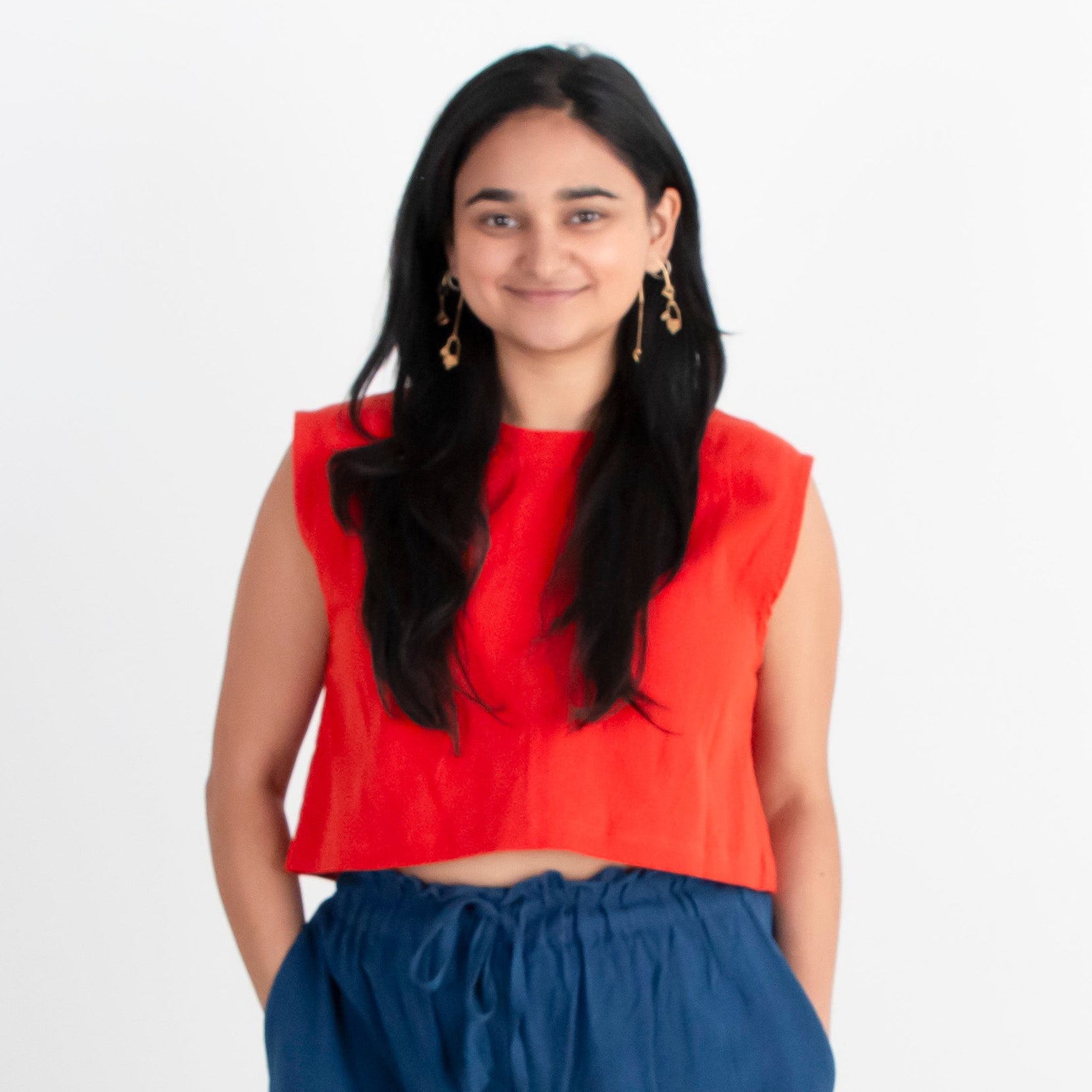 Woman wearing a red top and blue pants standing against a white background