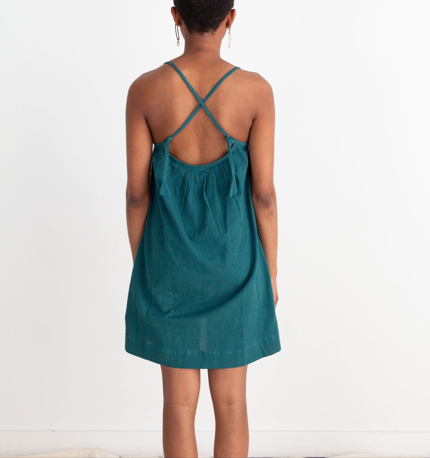 Person wearing a teal dress with criss-cross straps on a white background
