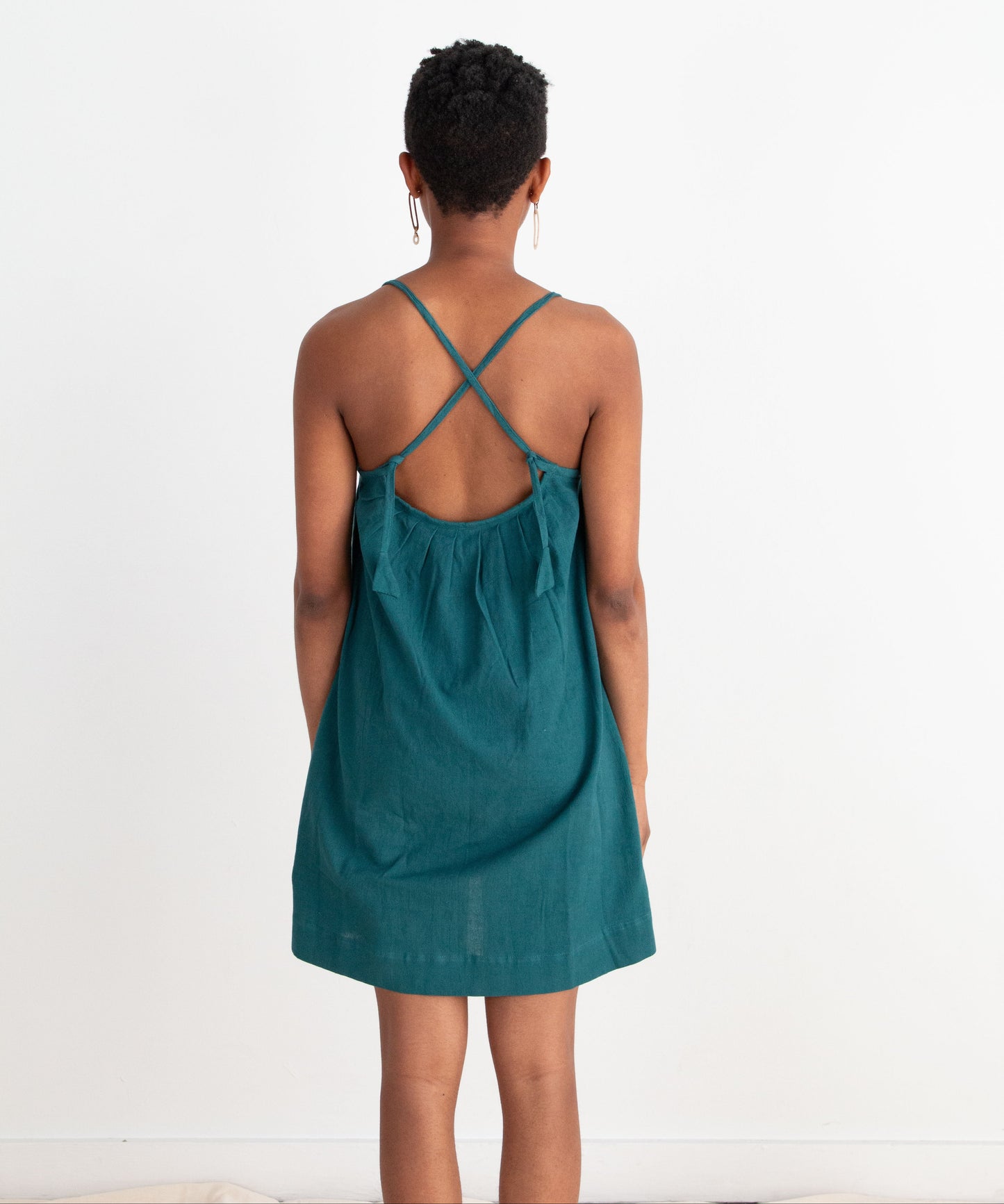 Person wearing a teal dress with criss-cross straps on a white background