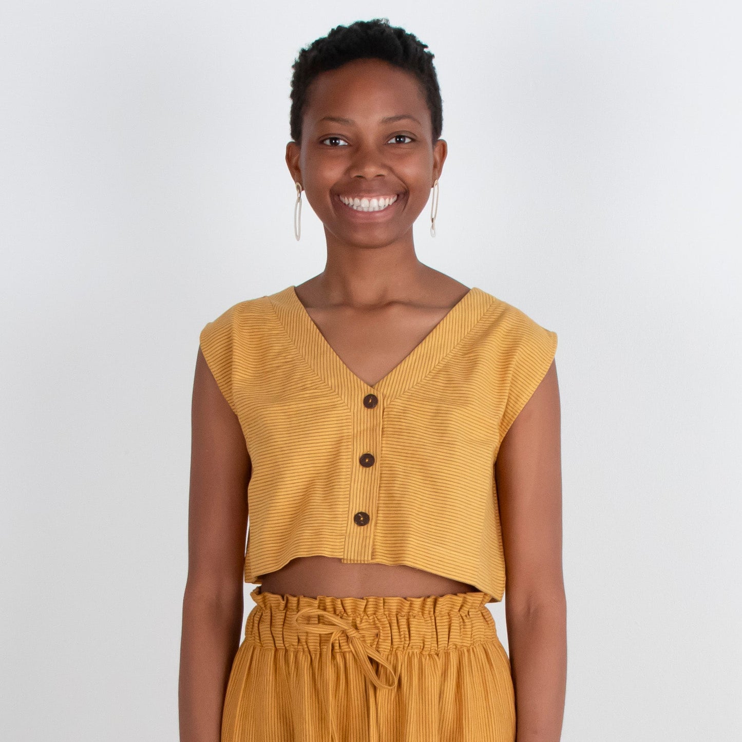 Woman wearing a mustard yellow outfit standing against a white background