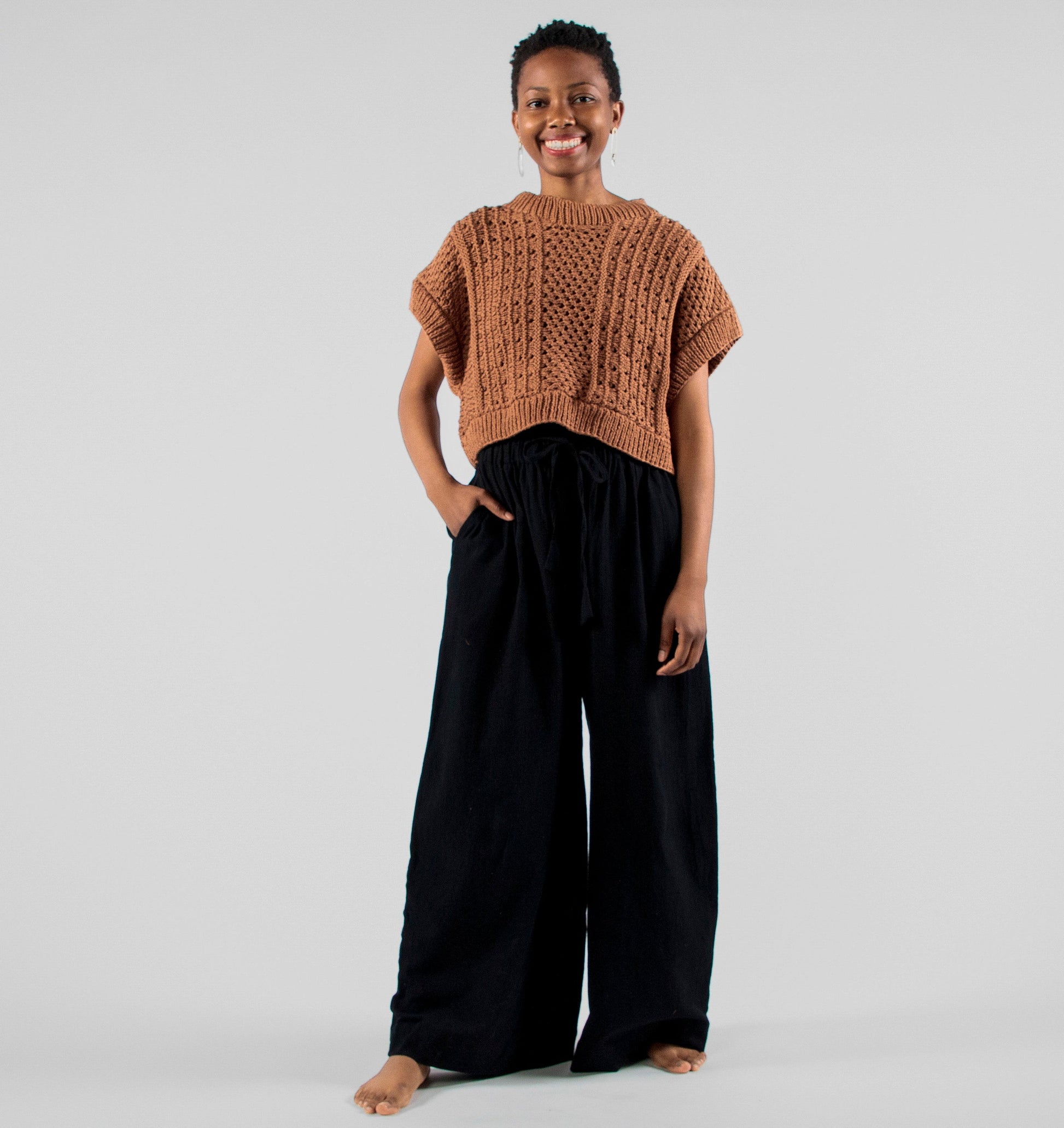 Person wearing a brown knitted top and black pants on a plain background