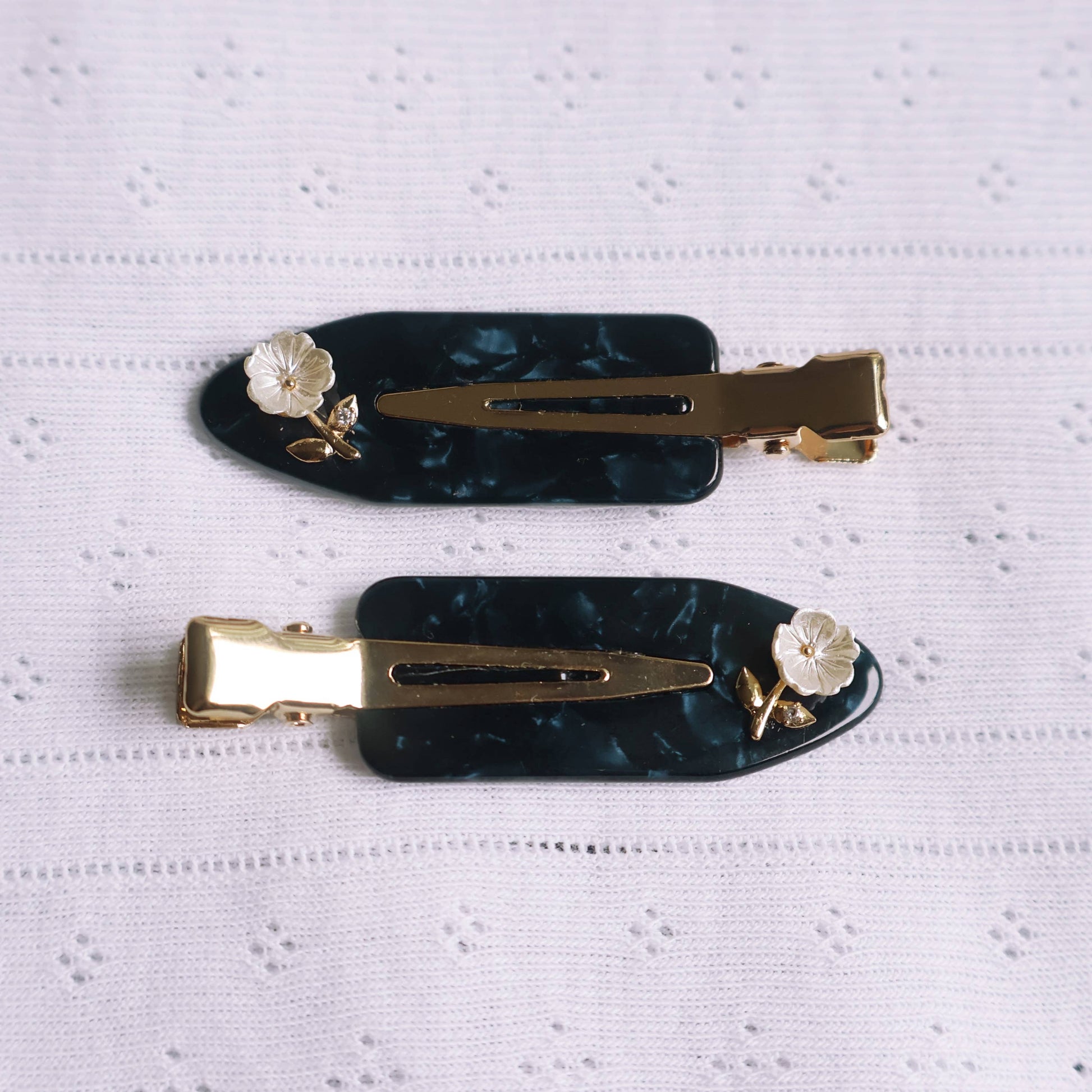 Two black hair clips with gold accents and floral decorations on a white textured background