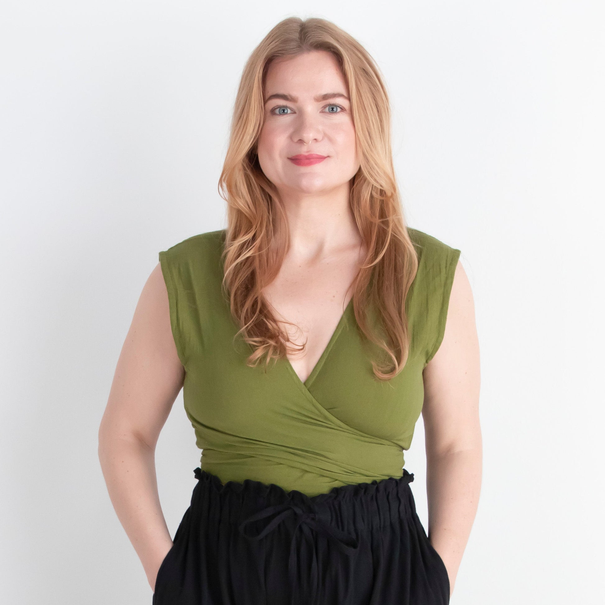 Woman wearing a green sleeveless top and black wide-leg pants against a white background