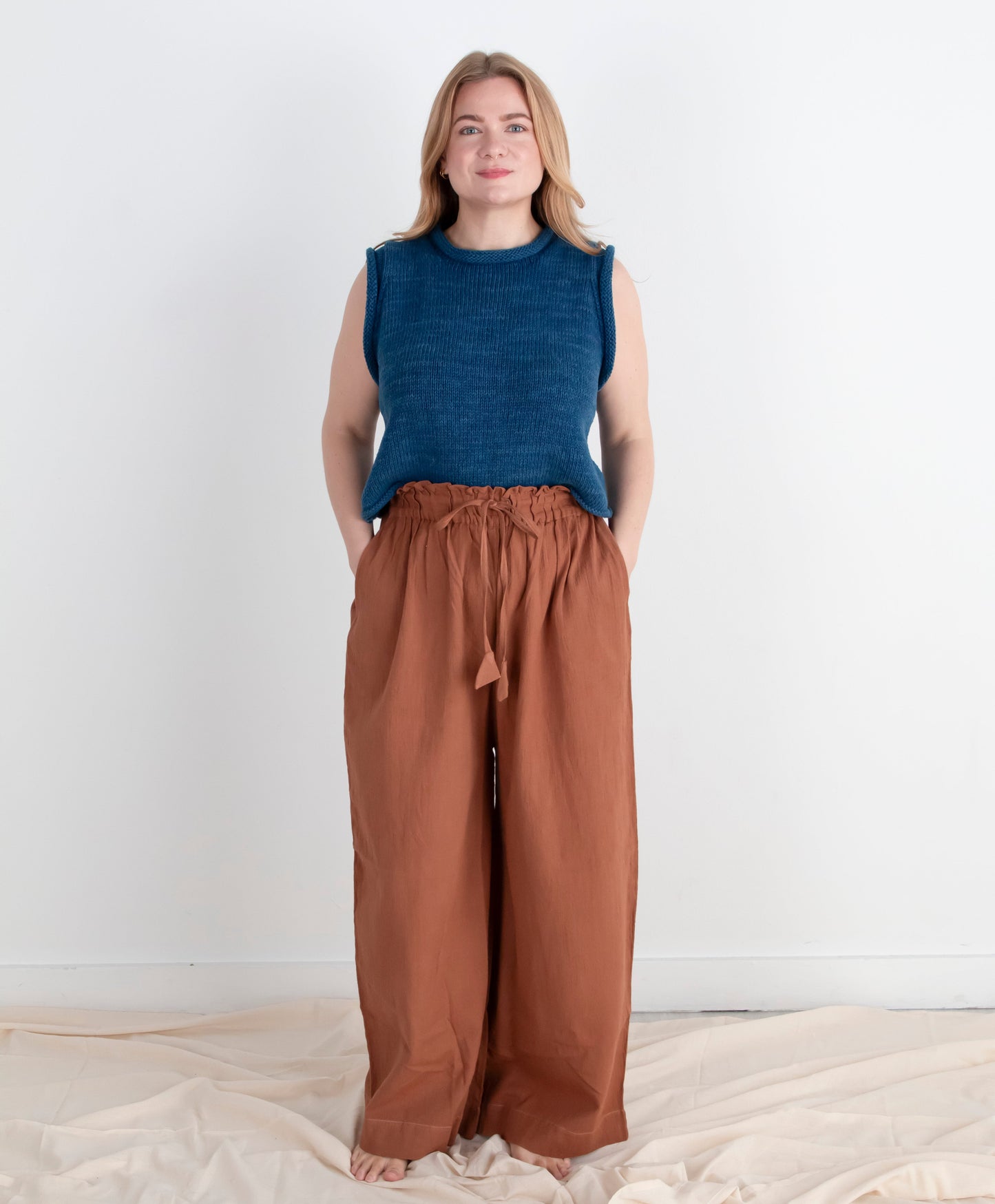 Woman wearing a blue sleeveless top and brown wide-leg pants on a white background
