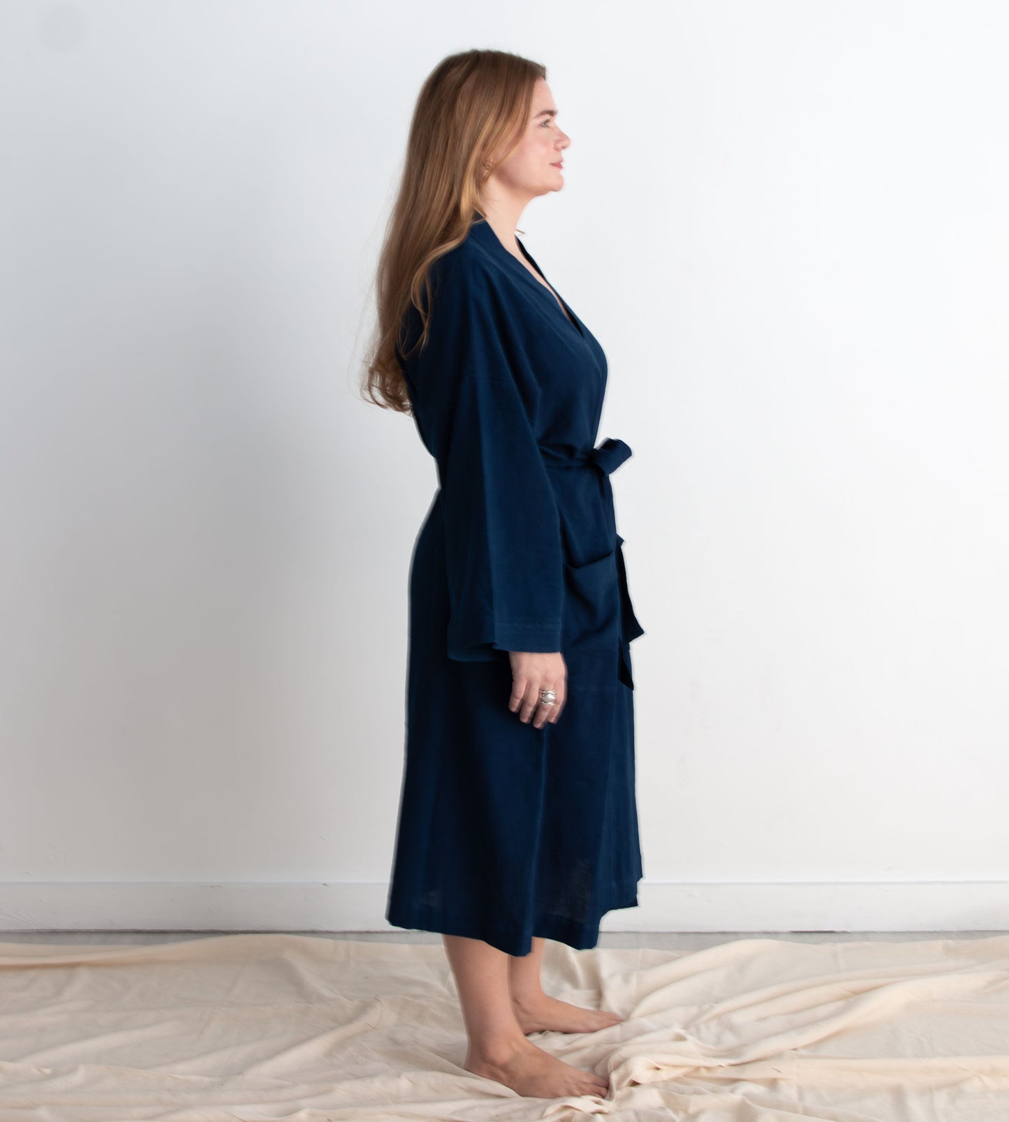 Woman wearing a navy blue robe standing against a white wall.