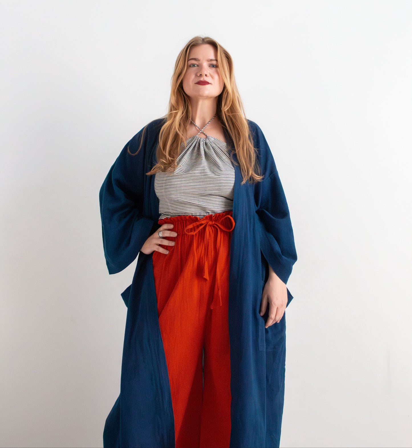 Woman wearing a blue robe over a pinstripe top and red pants on a white background