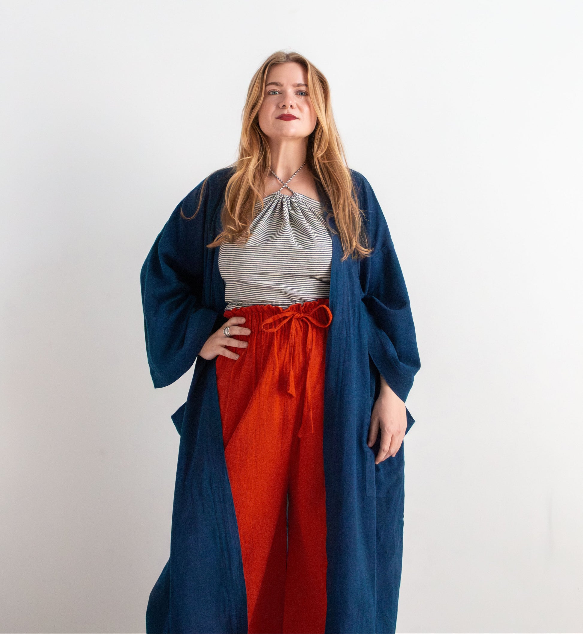 Woman wearing a blue robe over a pinstripe top and red pants on a white background