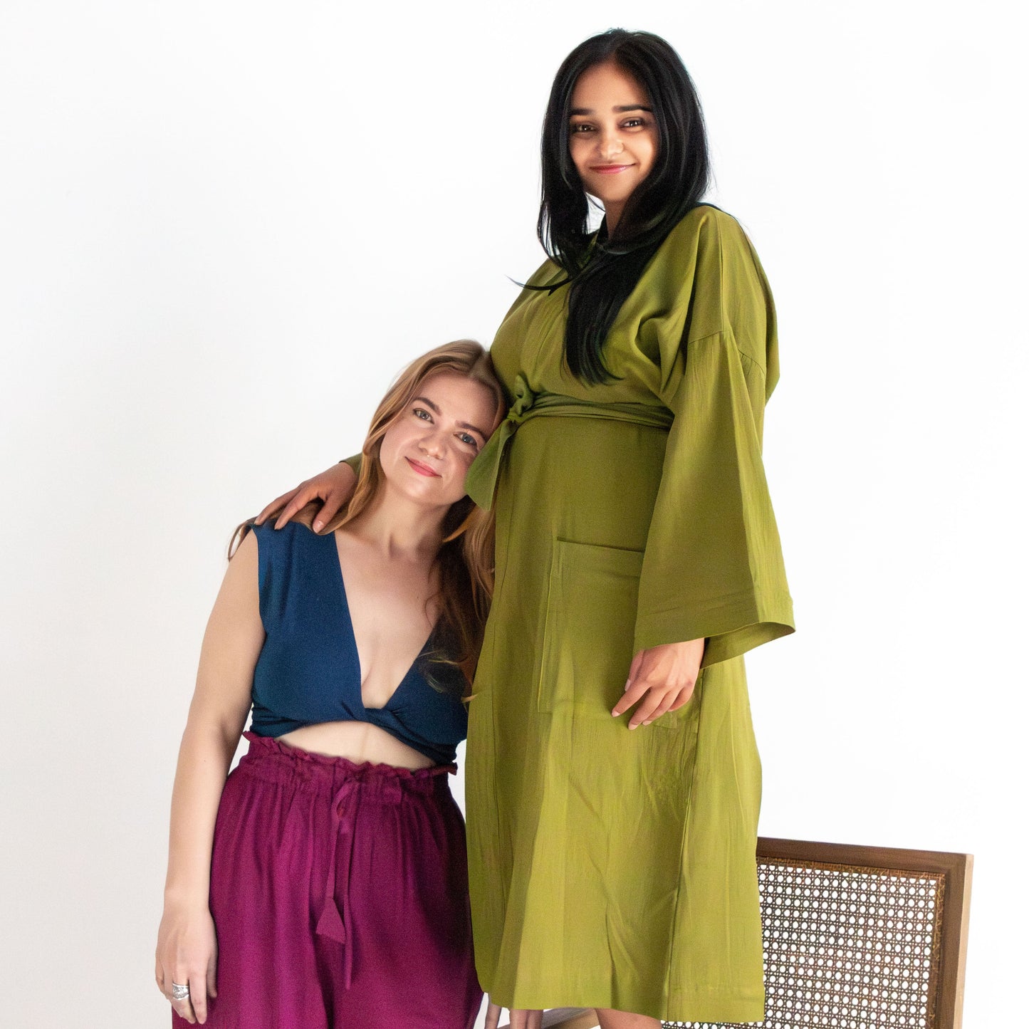 Two women wearing green and purple outfits on a white background