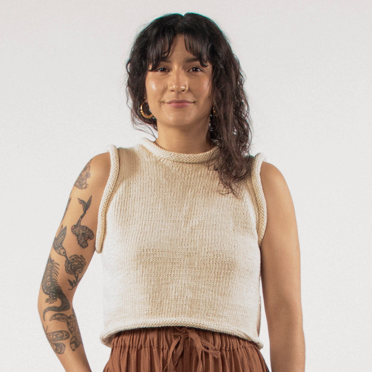 Woman standing in a studio with a white top and brown trousers