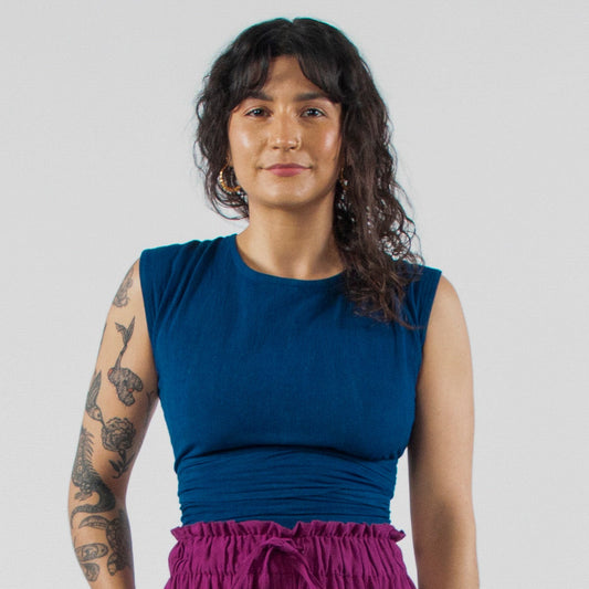 Woman wearing a blue sleeveless top and purple wide-leg pants standing on a white background.