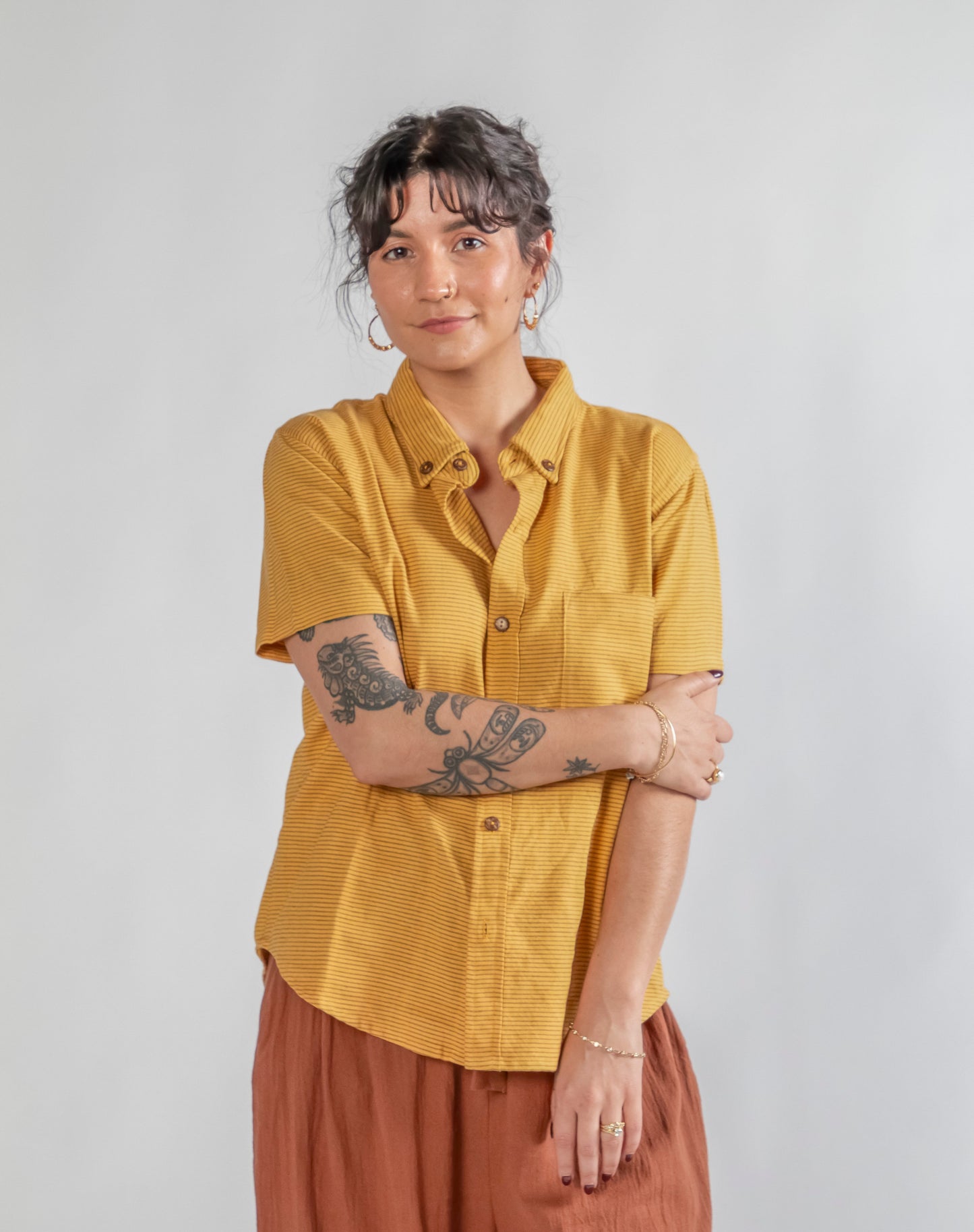 Person wearing a mustard yellow shirt and brown pants against a plain background