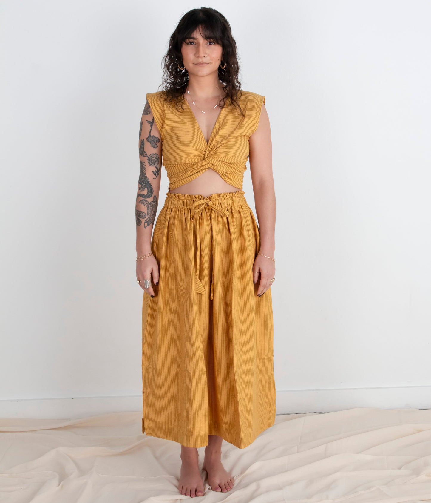 Woman wearing a mustard yellow top and skirt on a white background