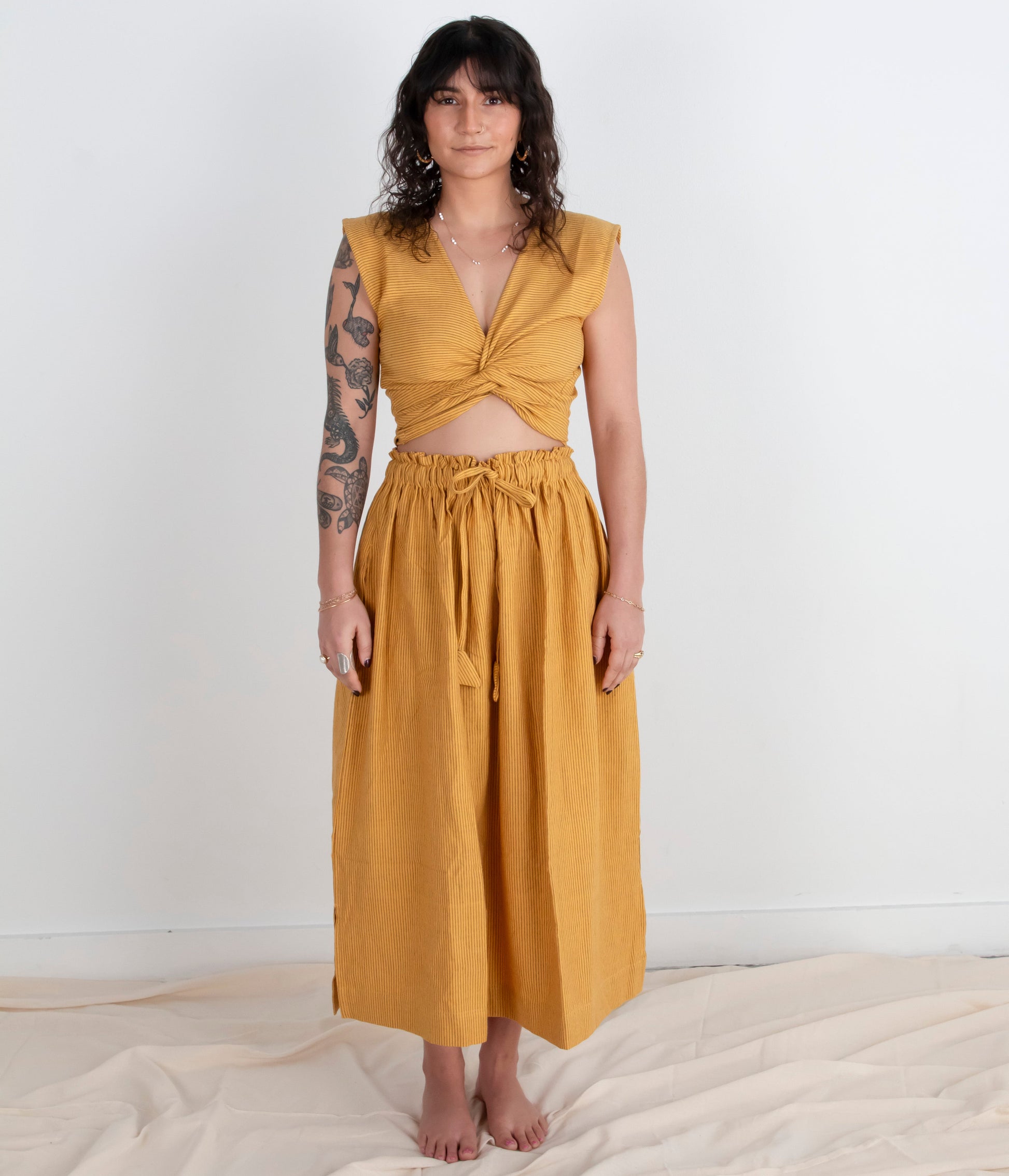Woman wearing a mustard yellow top and skirt on a white background