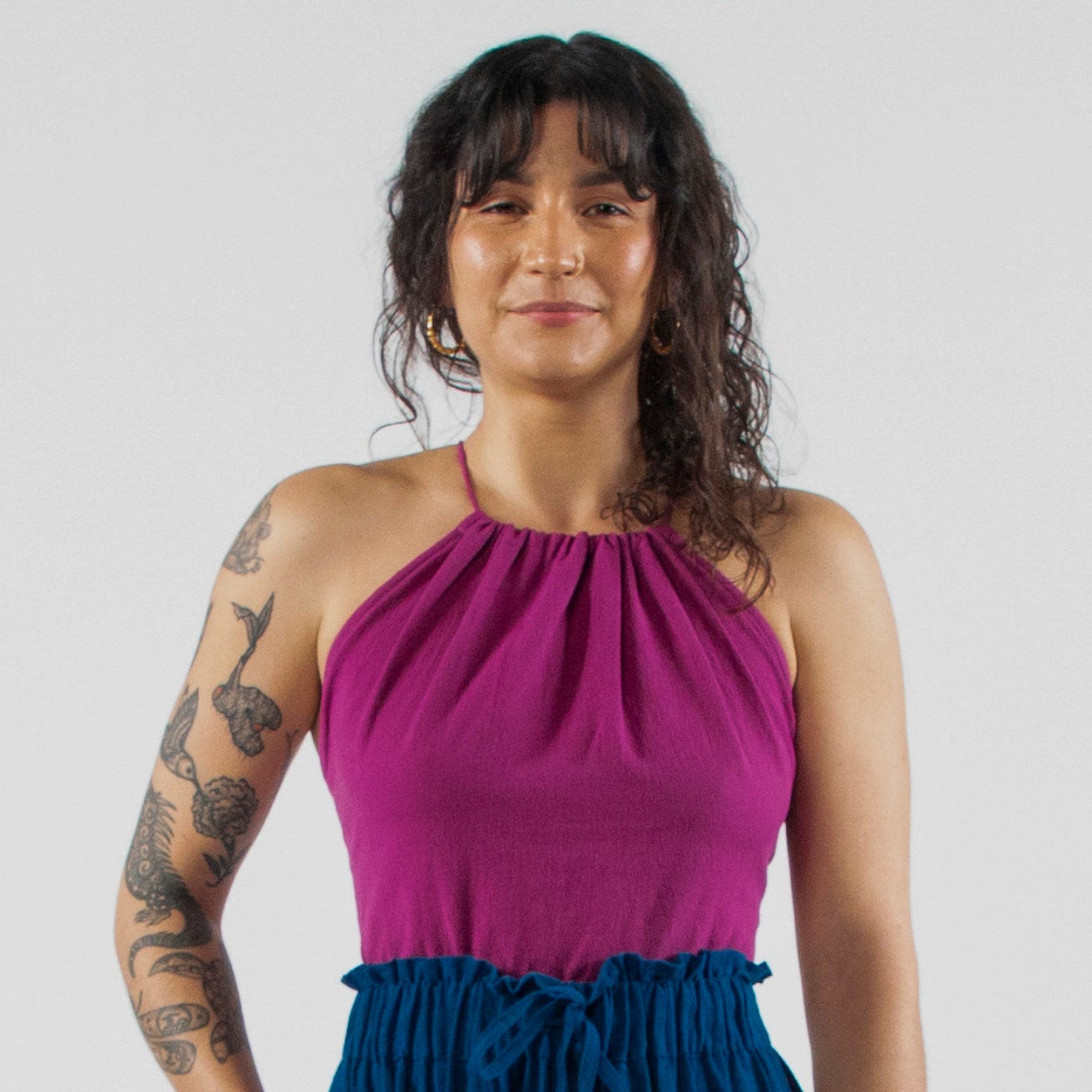 Woman wearing a purple top and blue pants standing on a white studio backdrop.
