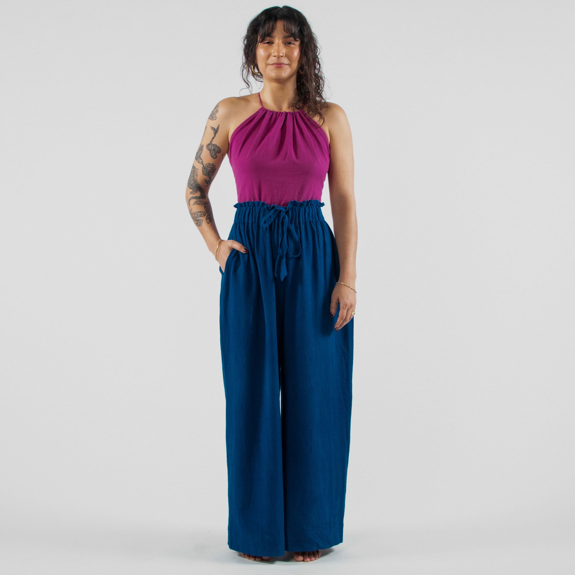 Woman wearing a purple top and blue pants standing on a white studio backdrop.
