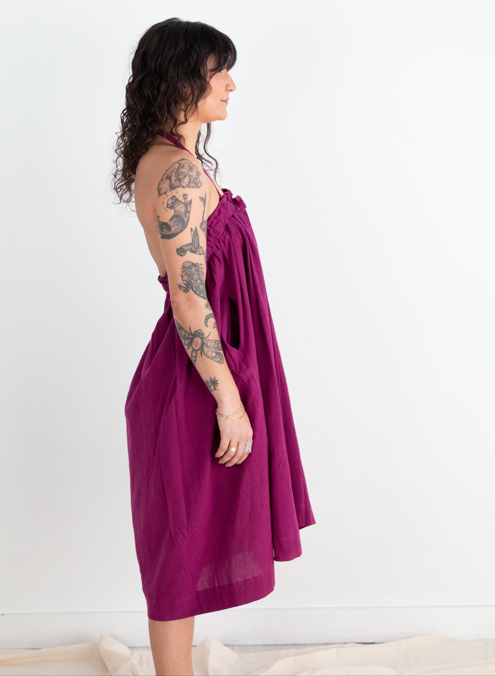 Woman wearing a purple dress with tattoos on her arms against a white background