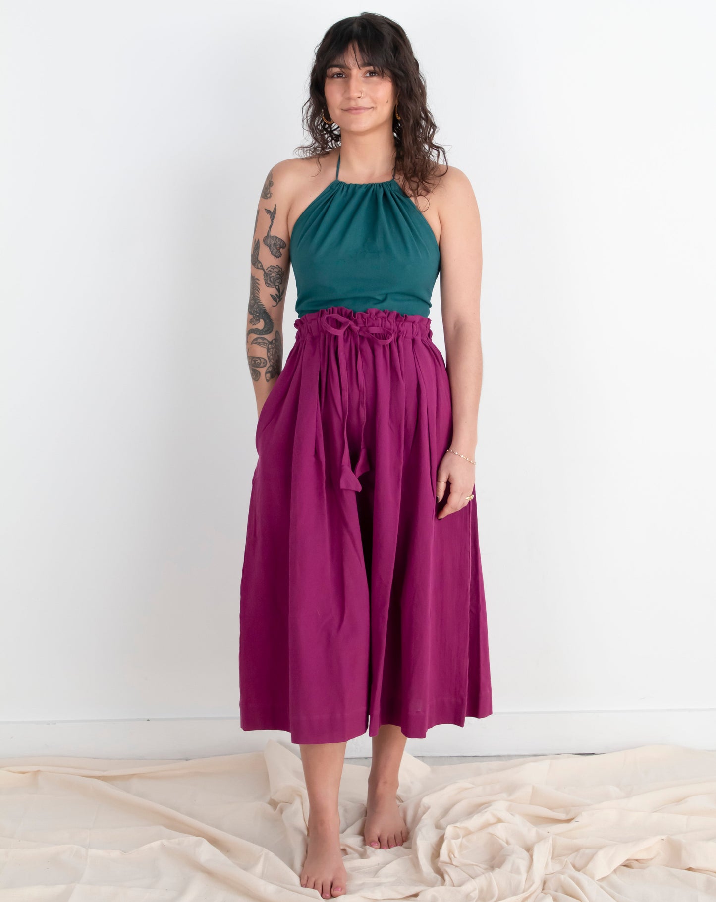 Woman wearing a teal top and magenta skirt against a white background