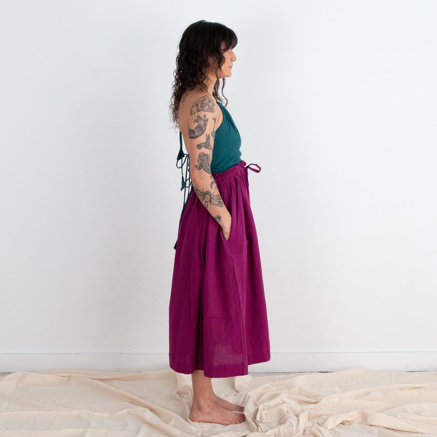 Woman wearing a teal top and magenta skirt standing against a white background