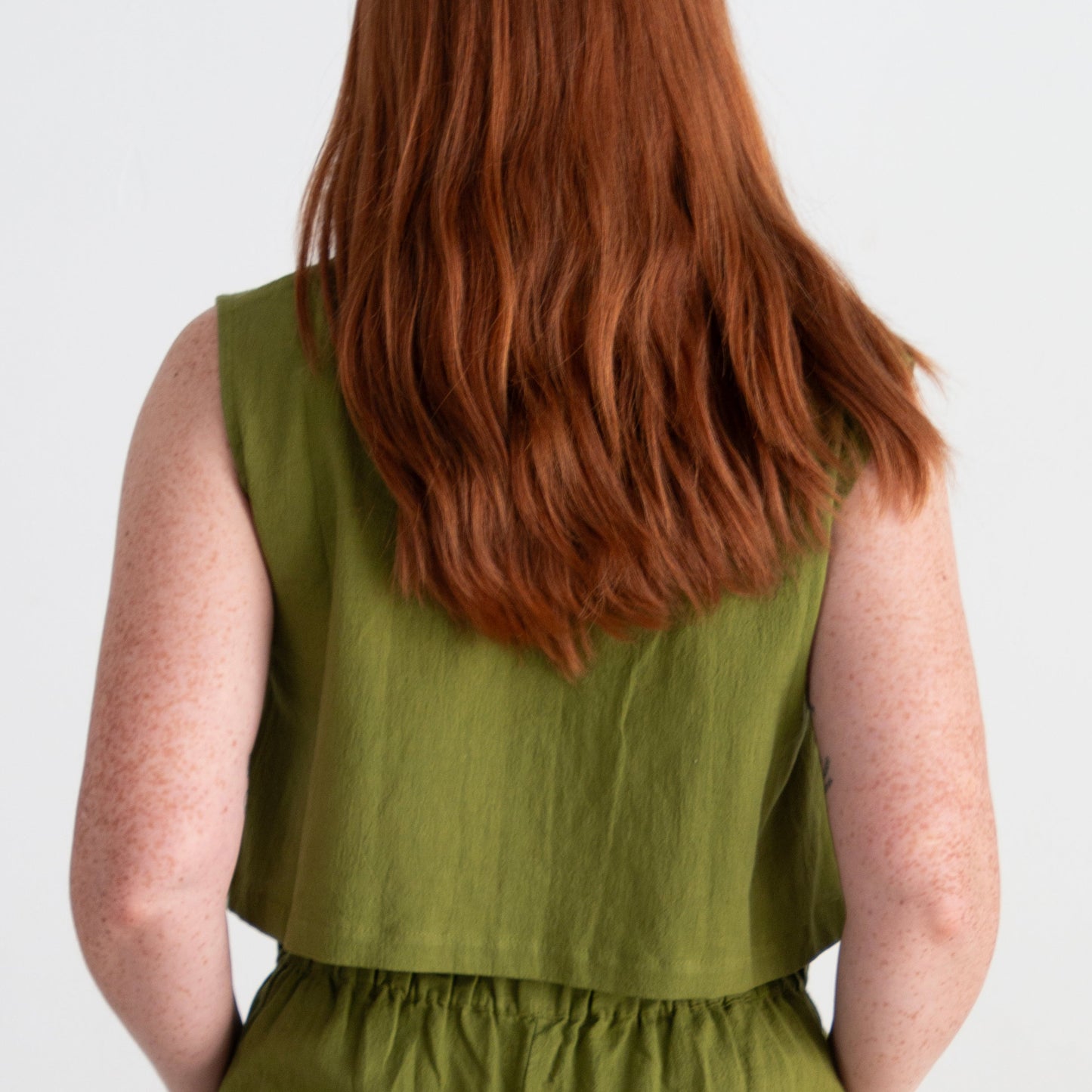 Person wearing a green sleeveless top and pants on a white background