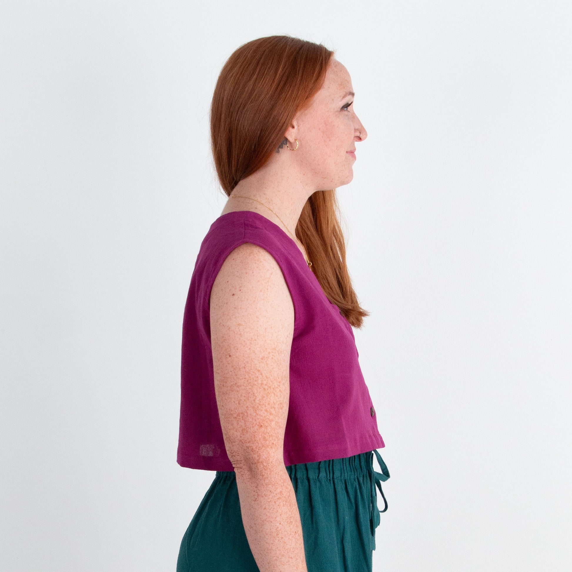 Woman wearing a purple top and teal pants against a white background