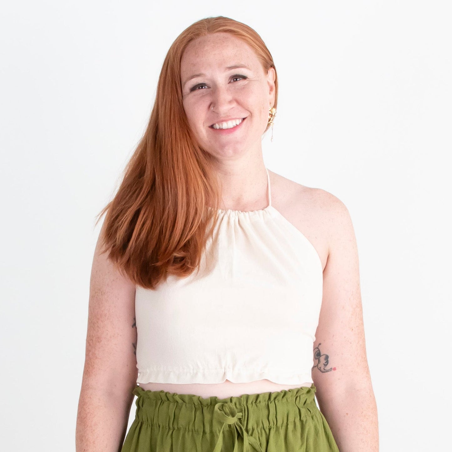 Woman wearing a white top and green pants standing against a white background