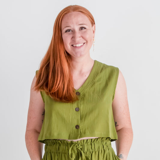 Woman wearing a green sleeveless top and high-waisted pants against a white background