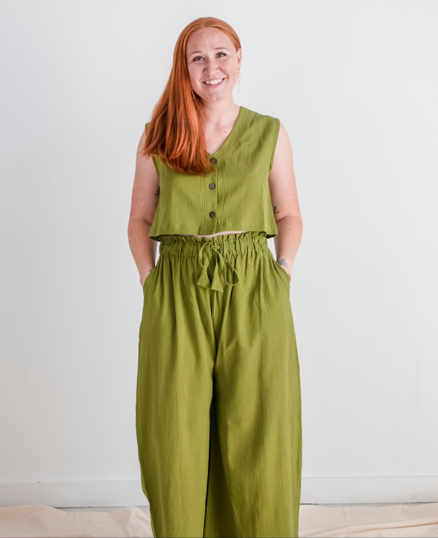 Woman wearing a green sleeveless top and high-waisted pants against a white background