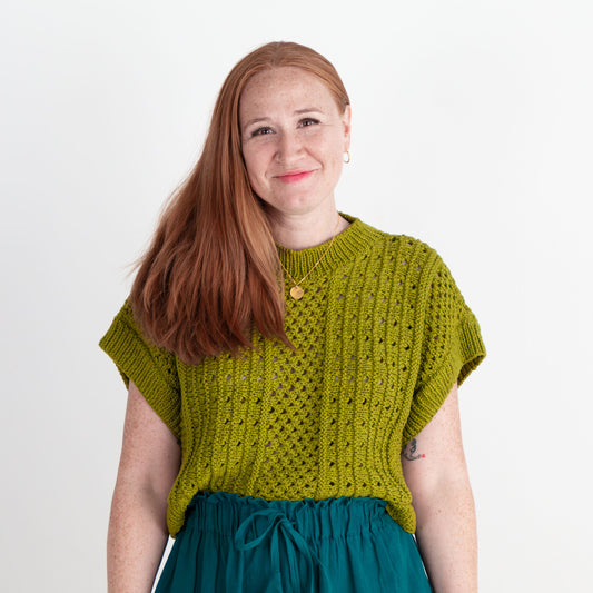 Woman wearing a green knitted top and teal skirt against a white background