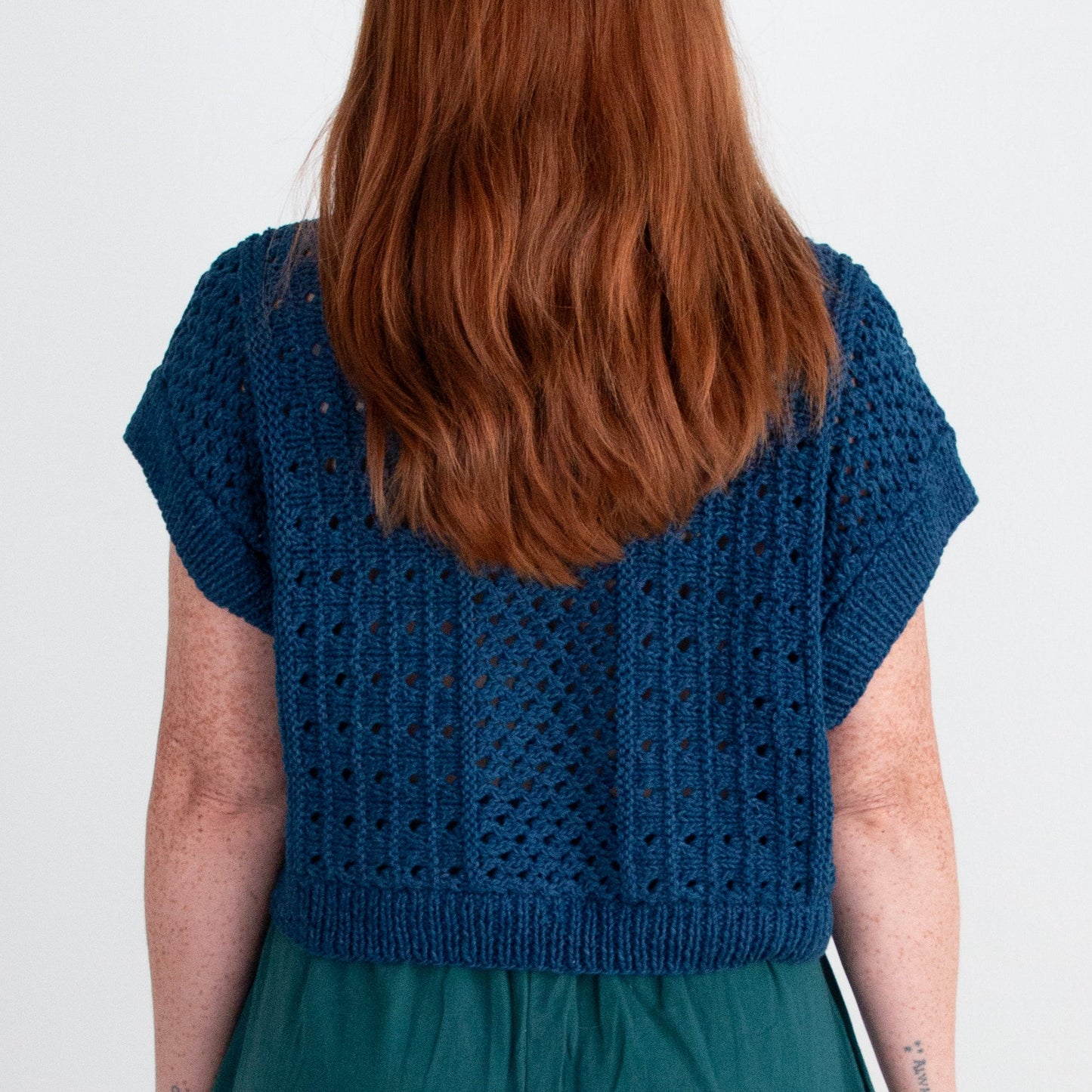 Person wearing a blue knitted top and teal pants on a white background
