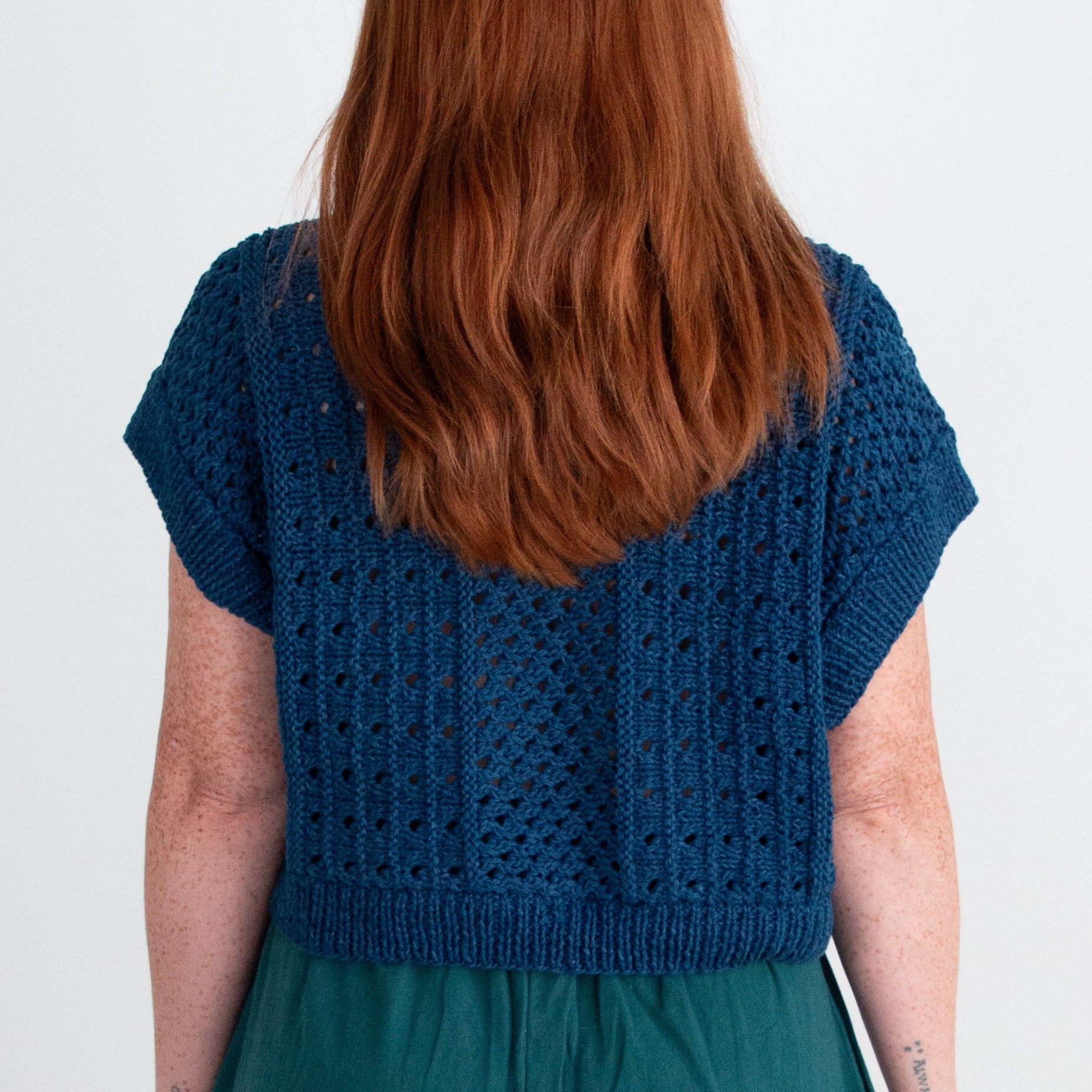 Person wearing a blue knitted top and teal pants on a white background