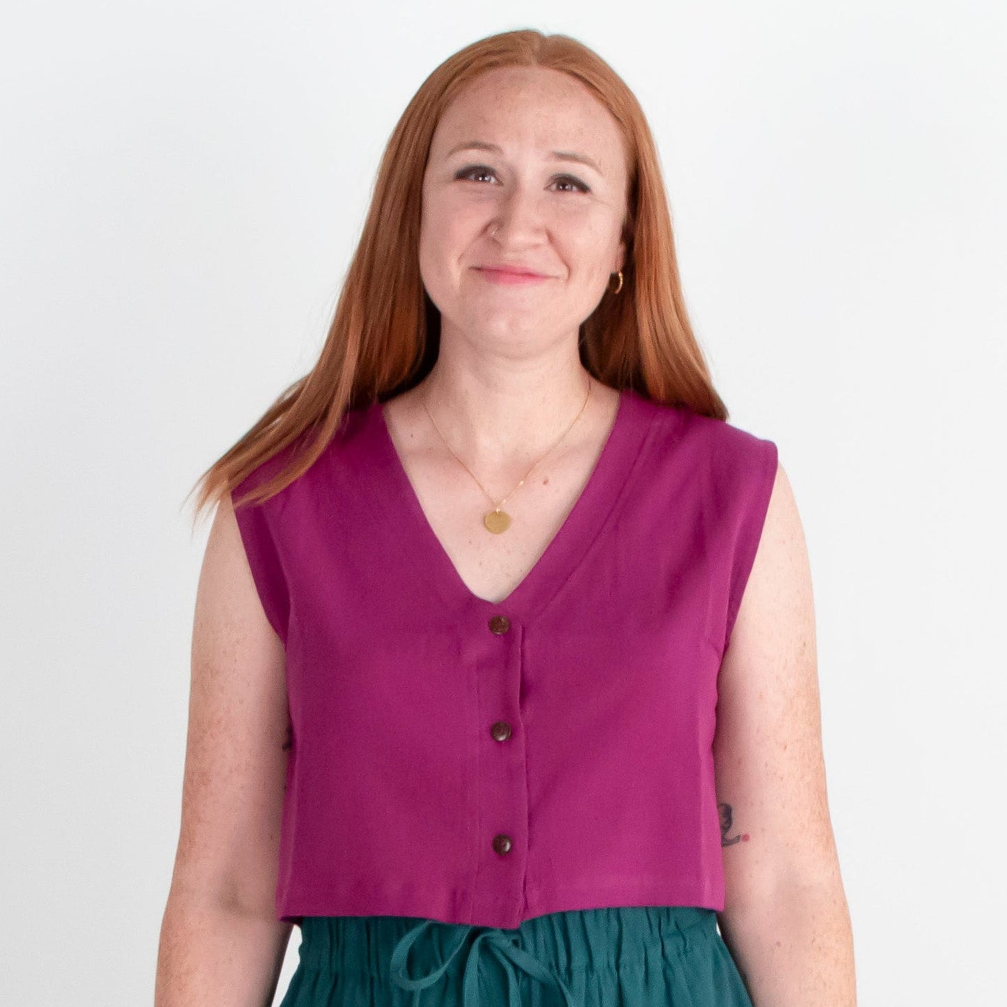 Woman wearing a purple sleeveless top and teal wide-leg pants on a white background