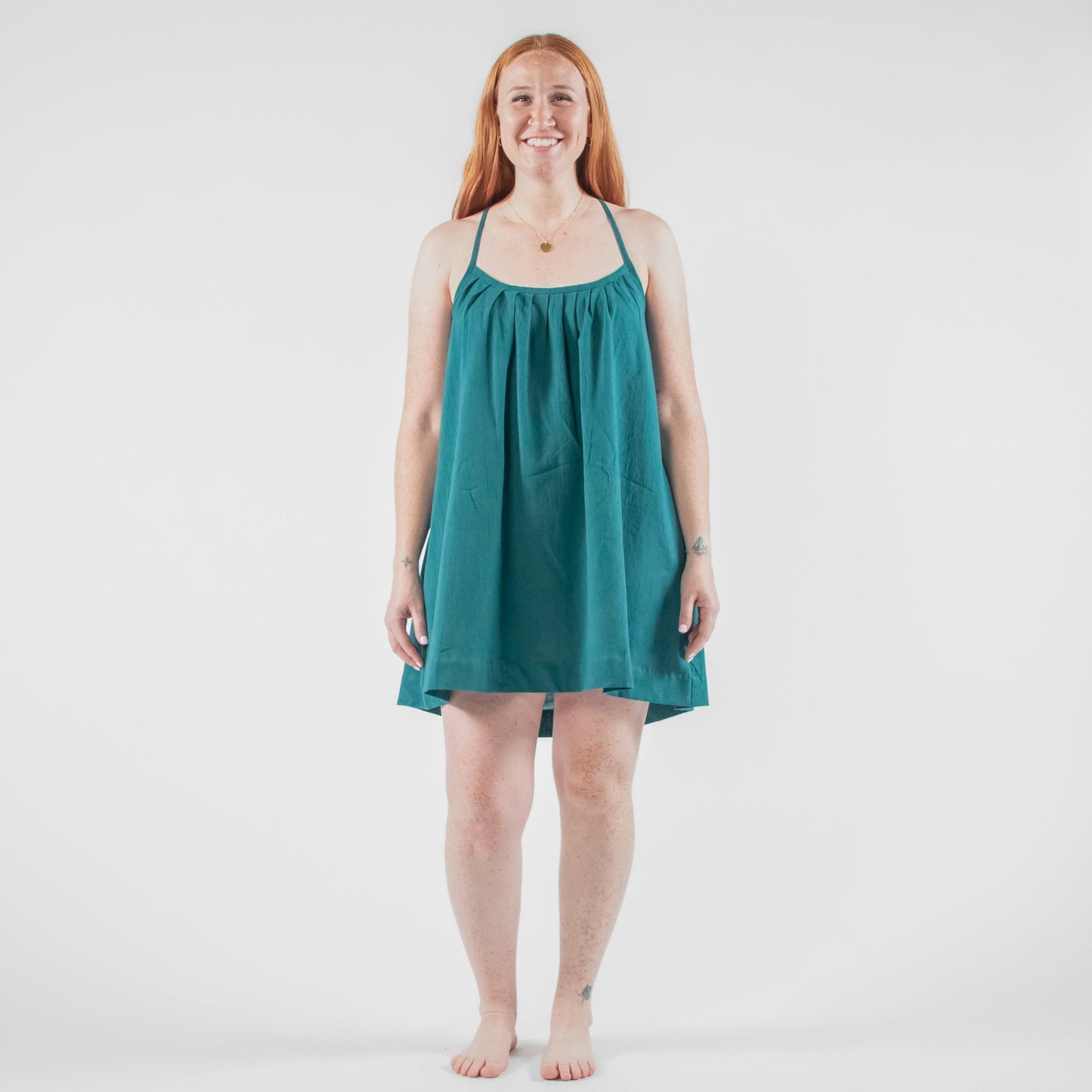 Woman wearing a teal dress standing on a white background in a photo studio.