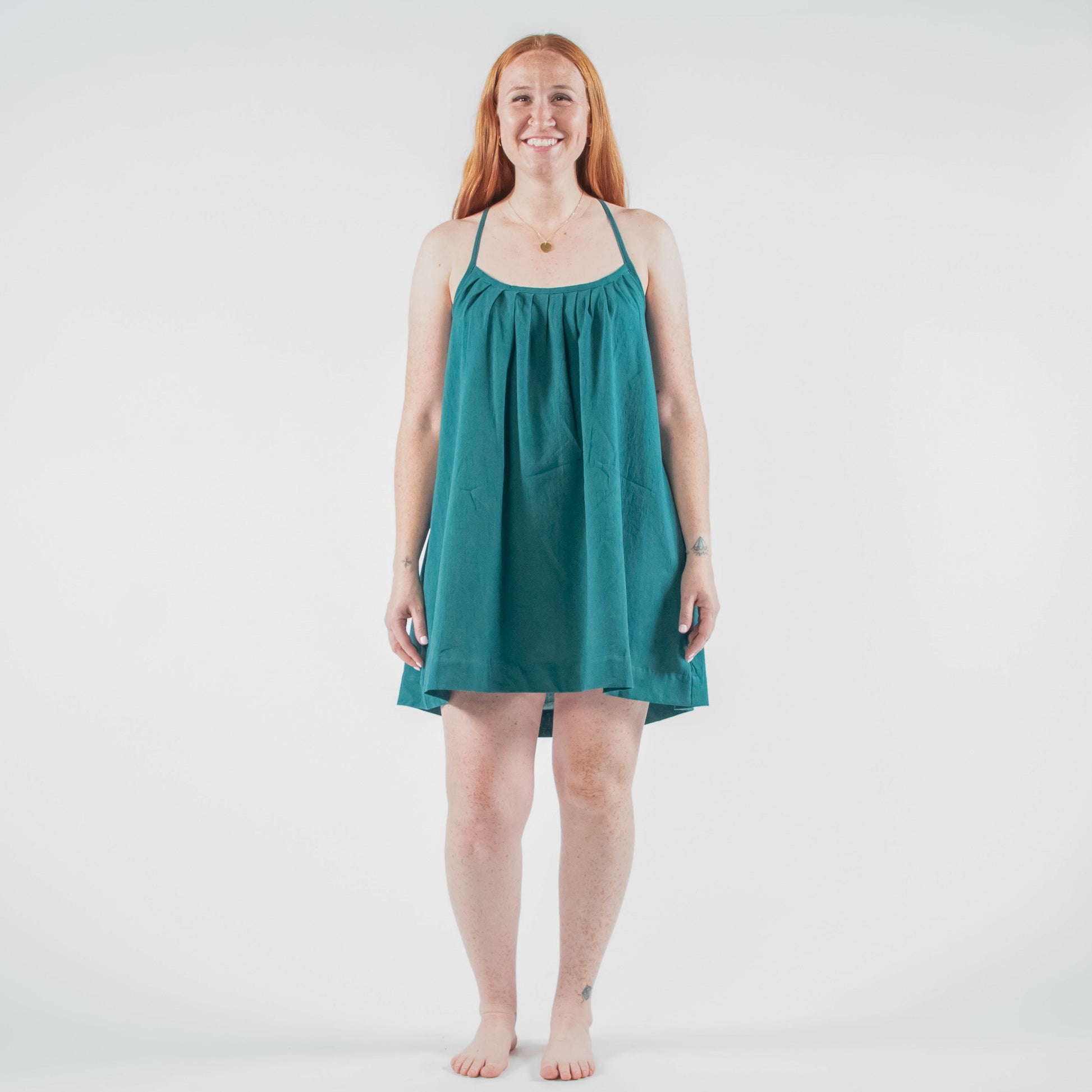 Woman wearing a teal dress standing on a white background in a photo studio.