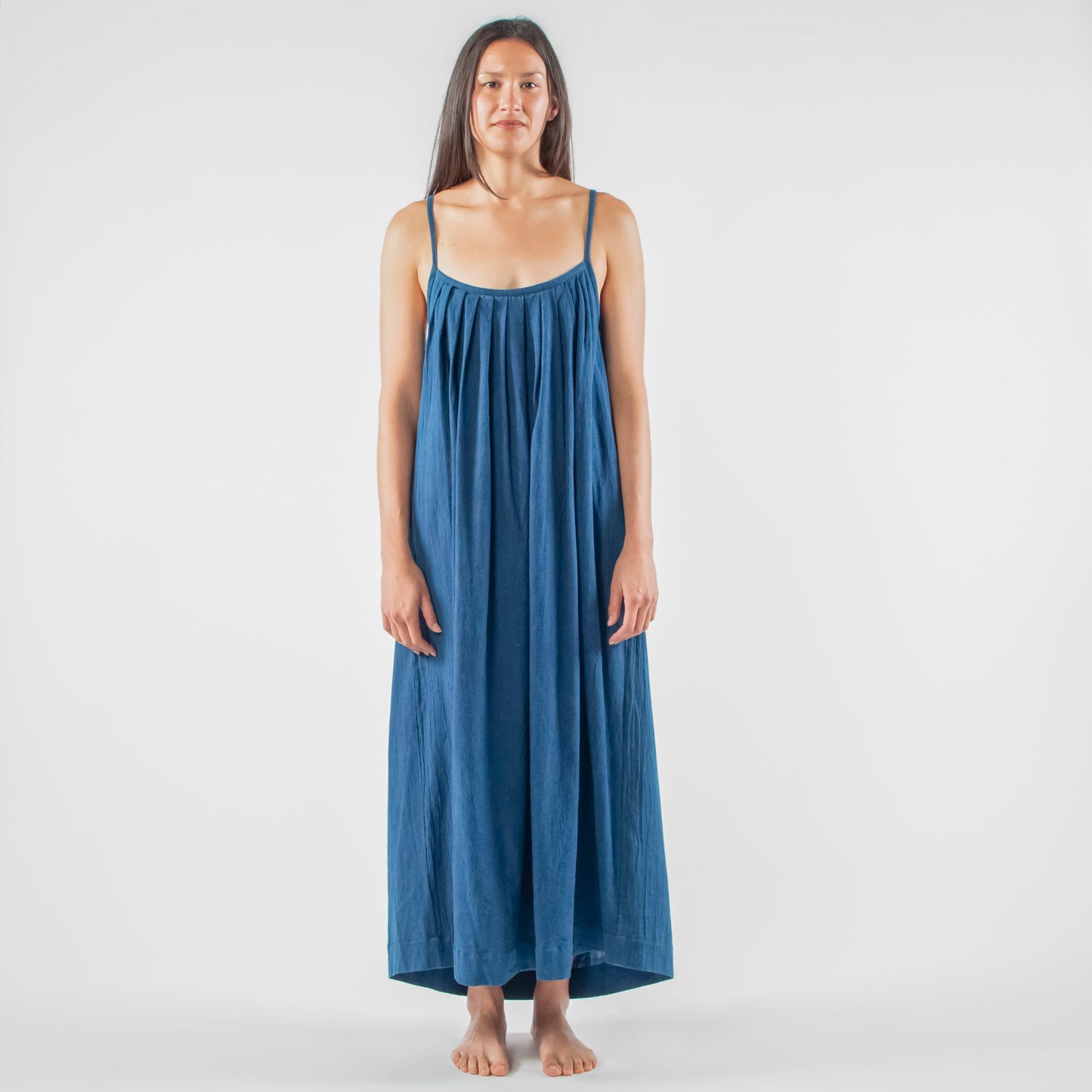 Woman wearing a blue dress standing on a white platform in a studio setting.
