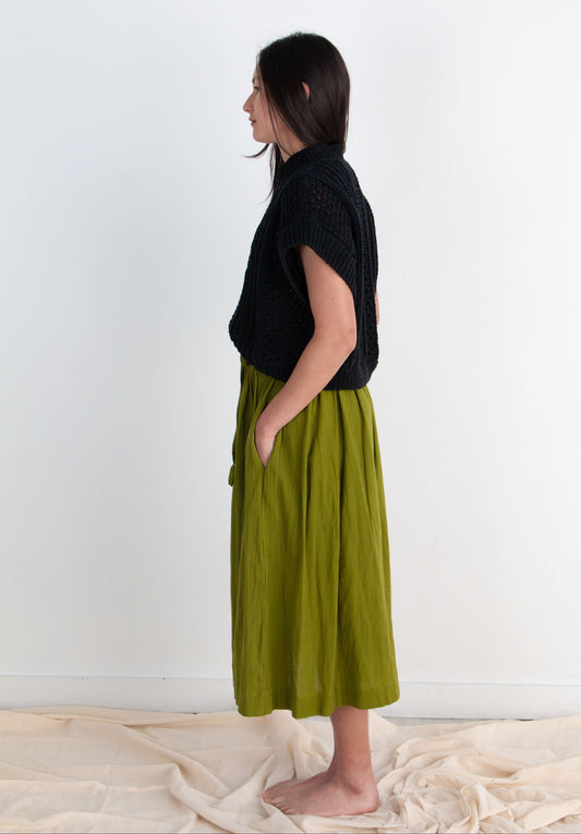 Woman wearing a black top and green skirt standing against a white background