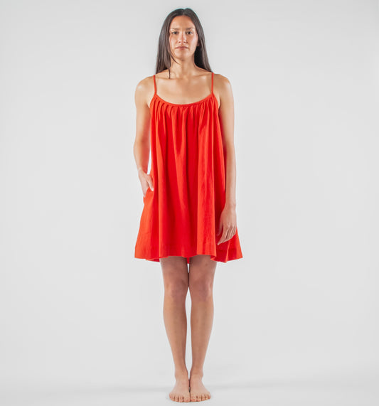Woman wearing a red dress standing on a white background with photography equipment around.